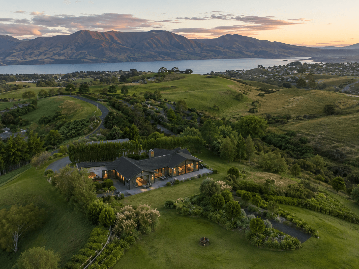 Aerial view of a home set among hills and a lakeside landscape at sunset